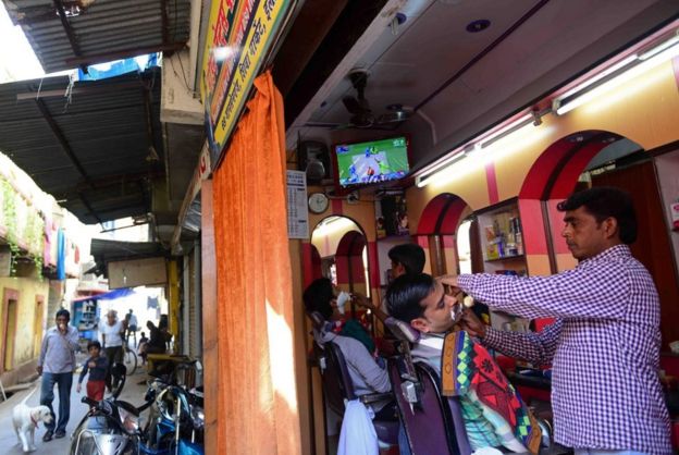 Indian customers get a shave at a barbershop at a television shows a live broadcast of the Cricket World Cup match between India and Pakistan, in Allahabad on February 15, 2015.