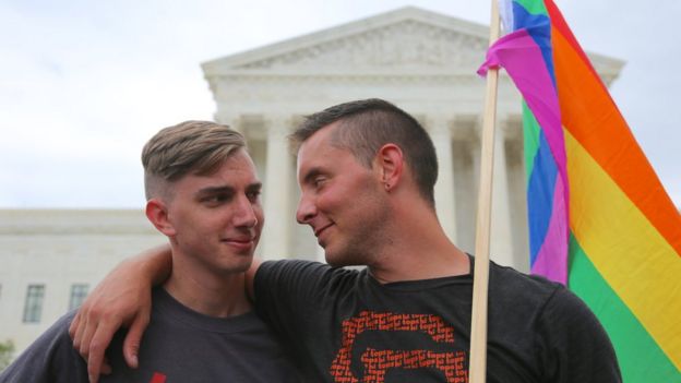 Two men stand outside the US Supreme Court with a rainbow flag