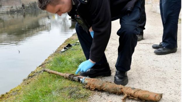 Police officers inspect a firearm on the canal bank after being removed from the canal as volunteers and staff from the Canal River Trust remove rubbish and some more bizarre objects that have been dumped into an east London canal