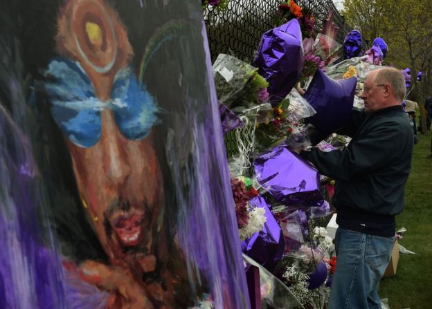 A Prince fans attaches flowers to a memorial wall as he pays his respects outside the Paisley Park residential in Minneapolis, Minnesota, 22 April