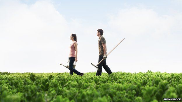 A man and woman walk through a field with gardening equipment