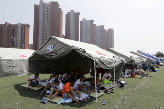 Locals rest under tents at a primary school, which has been turned into a shelter for people living nearby, near the site of the explosions at the Binhai new district, Tianjin, 13 August 2015