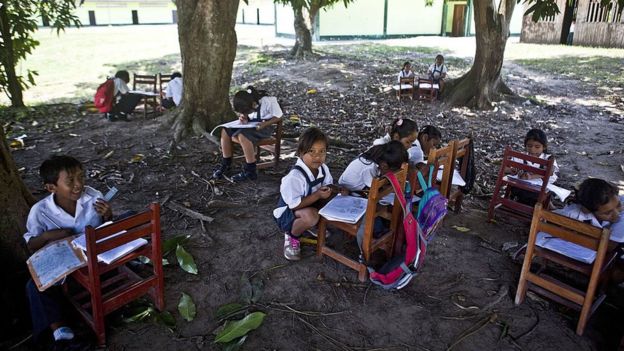 Niños en una escuela rural, estudiando sin carpetas.