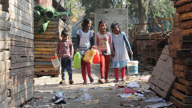 Indian children walk with containers to collect water from the hand pump, a ground water source of water , at the Azadpur area of in north Delhi, India (22 February 2016)