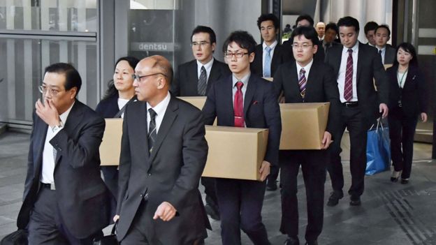 Funcionarios del Ministerio de Trabajo saliendo de la sede de Dentsu con cajas de cartón