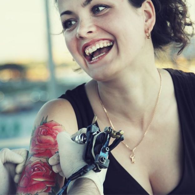 Mujer haciéndose tatuaje de flores rojas