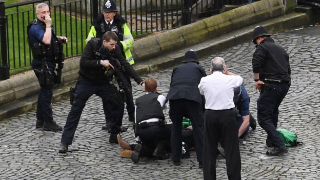 Un policía apunta un arma hacia un hombre tirado en el piso en la zona de acceso al Parlamento de Westminster.