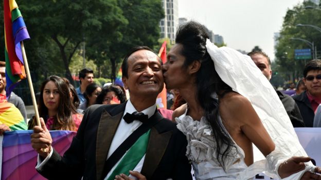 Desfile de una marcha gay en la que representan una boda de dos hombres, uno vestido de novia.
