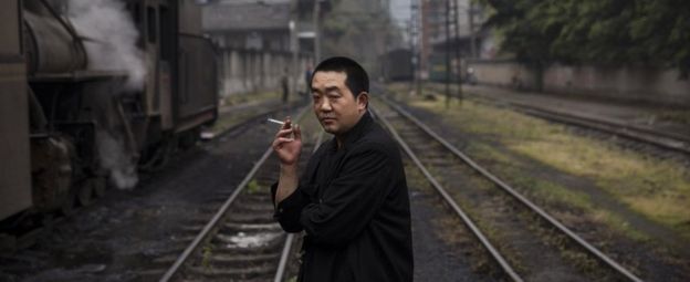 A railway engineer smokes as he waits next to a coal powered steam engine at a station in the town of Shixi , Sichuan Province