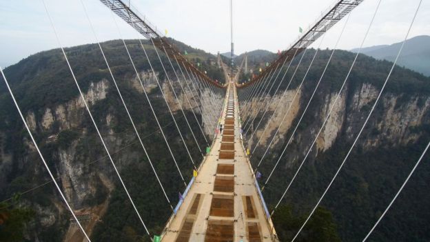 People walk across the framework of a 430-meter bridge under construction above a valley in Zhangjiajie in southern China's Hunan province