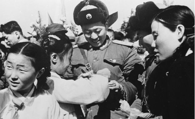 Korean girls present a member of the Chinese People's Volunteer Army with a bouquet of flowers prior to the mass withdrawal of Chinese troops from North Korea in 1958