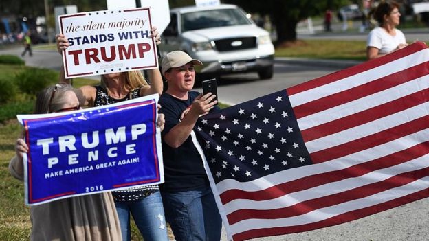 Trump supporters hold a US flag and a sign saying