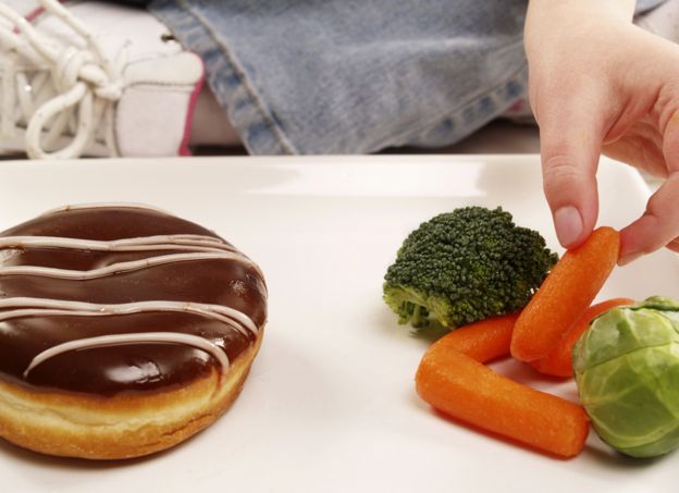 Person choosing between donut and vegetables