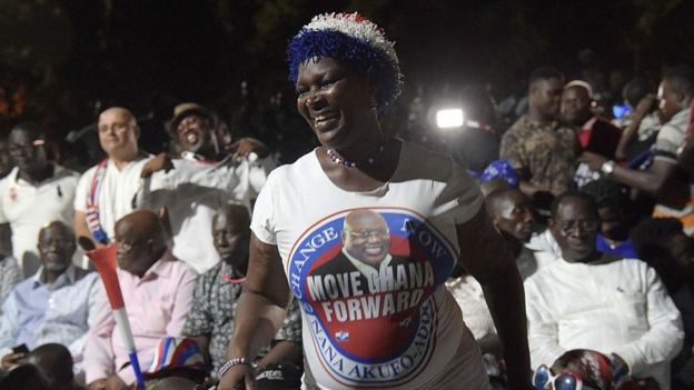 Woman wearing T-shirt of Ghana's president elect Nana Akufo-Addo celebrates, with the election winner himself visible in the background