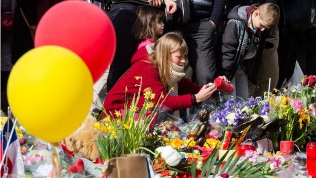 A woman lights a candle alongside floral tributes at the Place de la Bourse in Brussels (26 March)