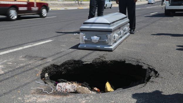 A coffin is placed next to a pothole in Mexico City