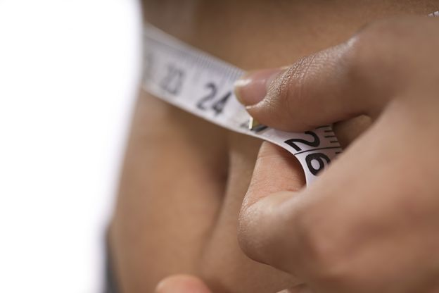 Close up of someone measuring waistline with a tape measure