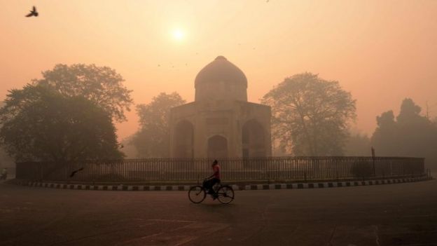 An Indian cyclist rides along a street as smog envelops a monument in New Delhi on October 31, 2016, the day after the Diwali festival.