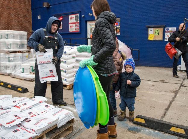 Woman with a child holding sleds and buying ice melter