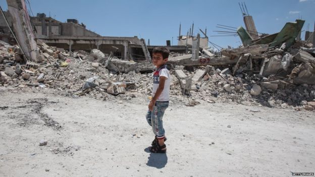 A boy walks past destroyed buildings in Kobane on 20 June