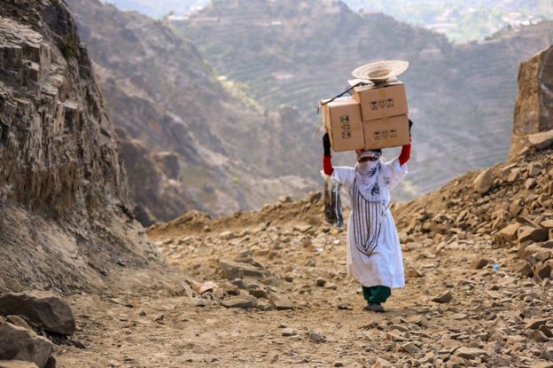 Woman carrying boxes over mountain paths to Taiz