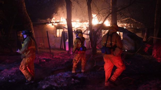Firefighters investigate a burning house, as the Thomas wildfire continues to burn in Carpinteria, California, 10 December 2017