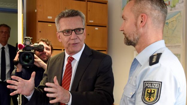 Mr de Maiziere at a police station, speaking to an officer 10 August 2016