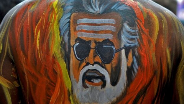 A fan with his body painted with an image of actor Rajinikanth is pictured outside a movie theatre showcasing the Tamil film 