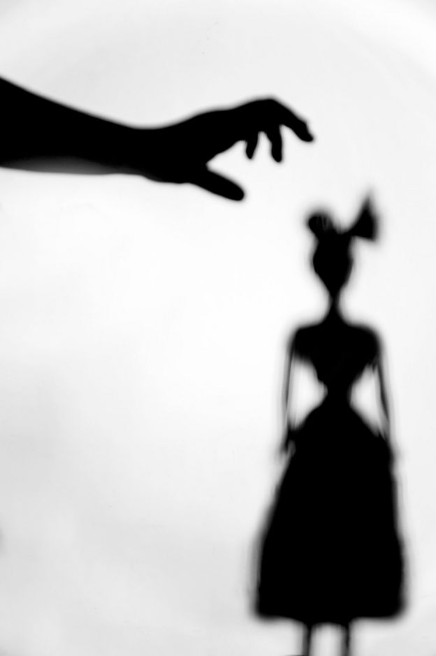 Ilustración de sombras. Una mano a punto de tomar a una mujer por la cabeza.