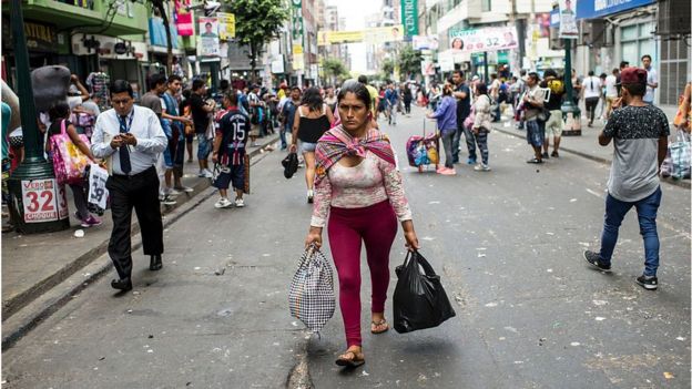 Mujer lleva paquetes en medio de una calle comercial popular