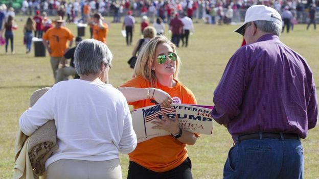 Una voluntaria de la campaña de Trump entrega volantes a unos seguidores del republicano en un mitin