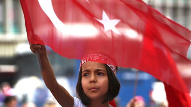 A Turkish girl wearing a headband bearing the name of Turkish president Recep Tayyip Erdogan waves her nation flags during a pro-government demonstration in front of the old parliament building, in Ankara, Turkey (July 20, 2016)