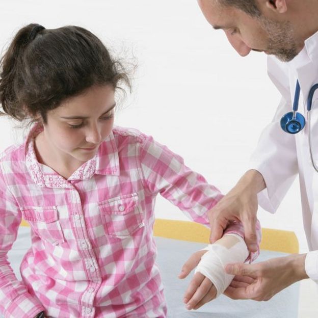 Médico atendiendo a una niña que tiene la muñeca enyesada