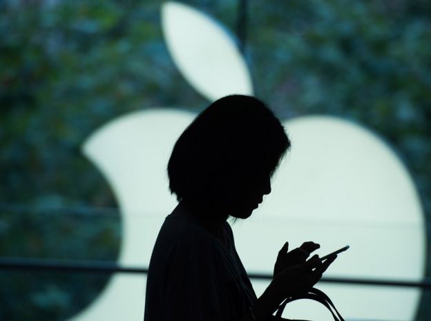 Mujer mira un teléfono delante de un logo de Apple