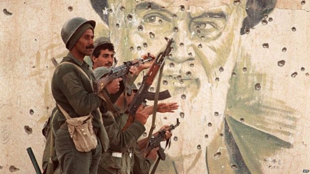 Iraqi soldiers pose in front of a bullet-marked mural of Ayatollah Khomeini in the strategic Faw peninsula of south-eastern Iraq (20th April 1988)