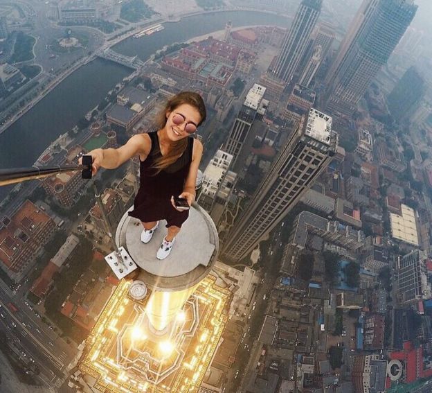 Angela Nikolau holding a selfie-stick on a small platform with the ground hundreds of metres below her