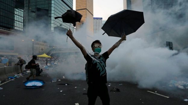 A protester raises umbrellas as tear gas is fired by riot police to disperse protesters outside the government headquarters in Hong Kong (28 September 2014)