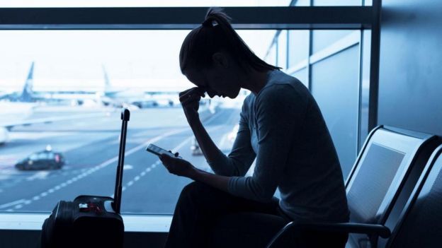 Una mujer en un aeropuerto, viendo su teléfono