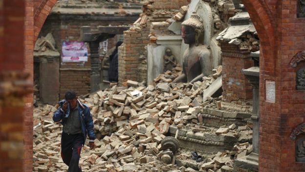 A man cries as he walks on the street while passing through a damaged statue of Lord Buddha a day after an earthquake in Bhaktapur, Nepal April 26, 2015