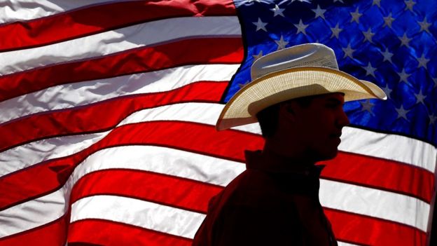 Man in a cowboy hat silhouetted against the US flag