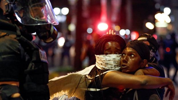 Two women embraced while looking at a police officer in Charlotte, North Carolina during a protest on 21 September
