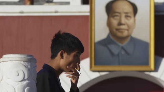 A man smokes in front of a portrait of Chairman Mao