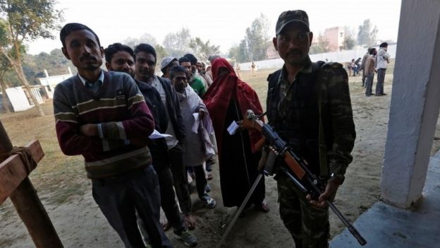 People queue to cast their vote as a security personnel stands guard at a polling station during the state assembly election in Hapur, in the central state of Uttar Pradesh (11 February 2017)