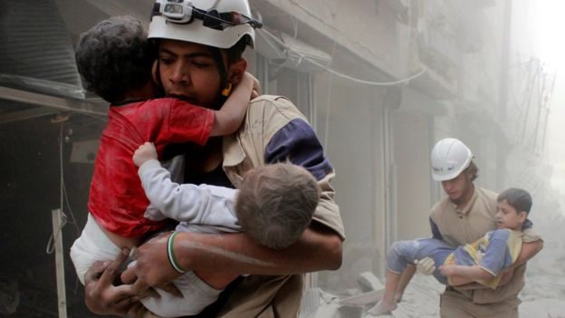 A member of Syria's White Helmets carries children to safety after a bomb strike