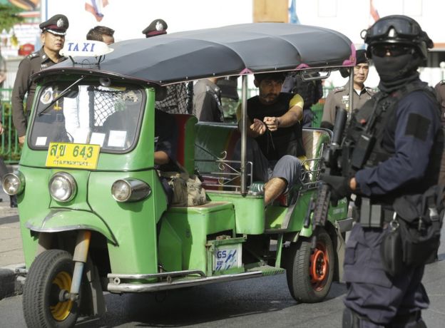Police officers escort a key suspect in last month's Bangkok bombing, yellow shirt, identified by Thai police as Yusufu Mieraili, traveling on a Chinese passport, sits on a three wheel taxi outside Hua Lamphong railway station during a re-enactment for the 17 August bombing at Bangkok's popular Erawan Shrine that left 20 people dead and more than 120 injured, Wednesday, 9 September 2015