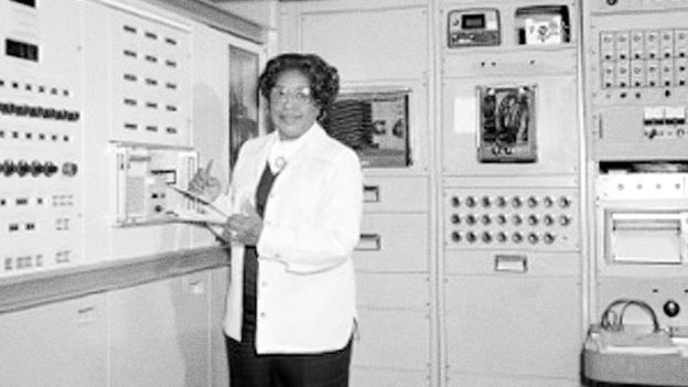 Mary Jackson holds a clipboard standing by a large computer