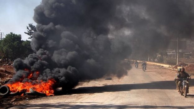 Rebel fighters from the Jaish al-Fatah (or Army of Conquest) brigades drive past burning tyres at an entrance to Aleppo, in the south-western frontline near the neighbourhood of Dahiyet al-Assad (03 November 2016)