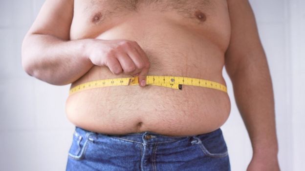 Hombre con sobrepeso midiéndose la cintura