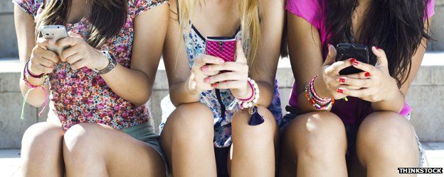 Girls sitting in a row using mobile phones