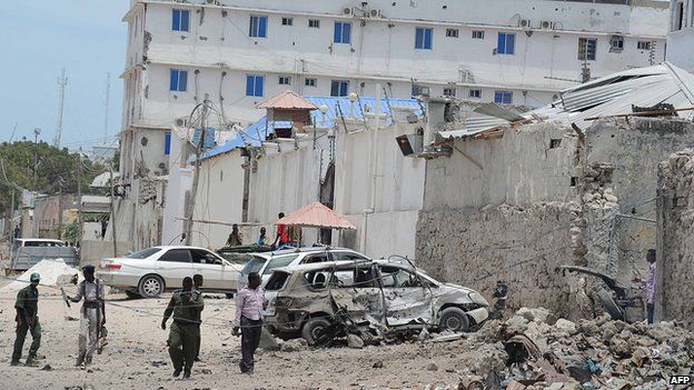 Somali government soldiers walk around a destroyed car at the site of car bomb blast in front of the Makka Al Mukarrama Hotel in Mogadishu, on 15 March, 2014.